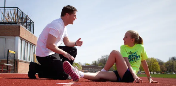 Coach supports an injured athlete on the track, emphasizing sports and performance psychology in recovery and resilience.